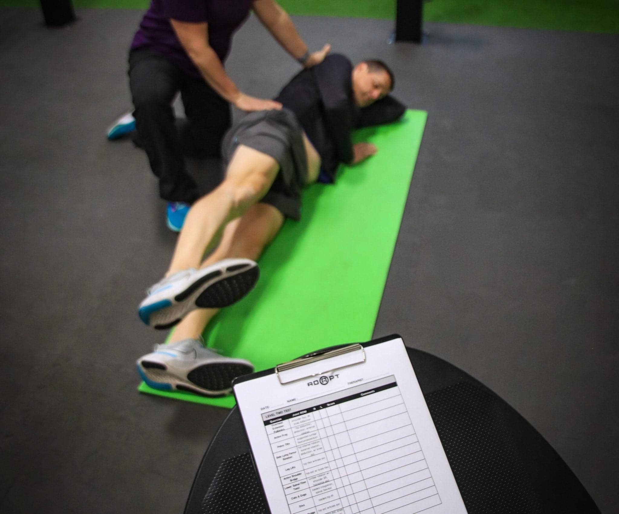 ADAPT PT performing manual therapy with a movement assessment clipboard visible