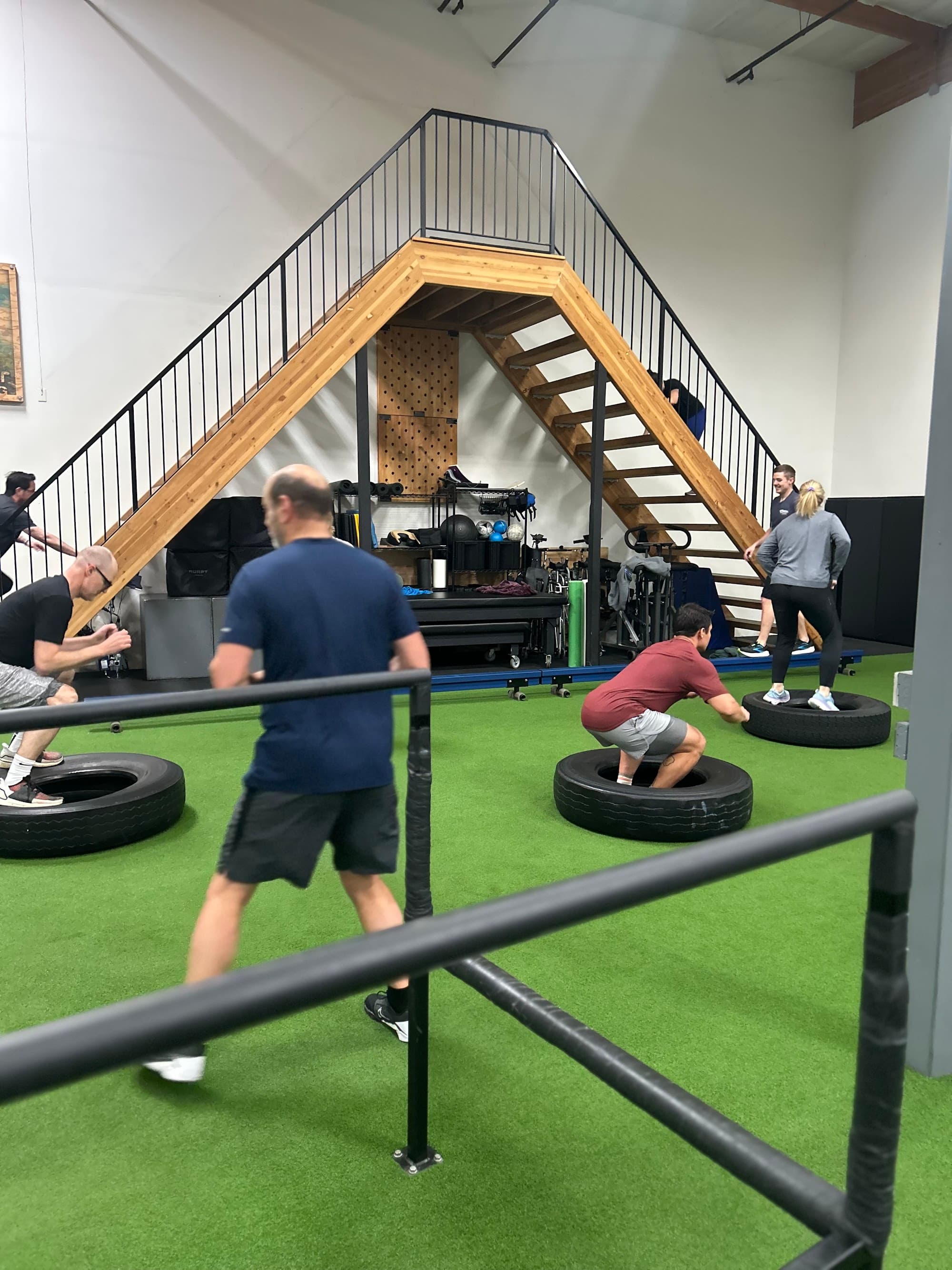 Athletes squat-jumping over tires under the ADAPT A-frame staircase